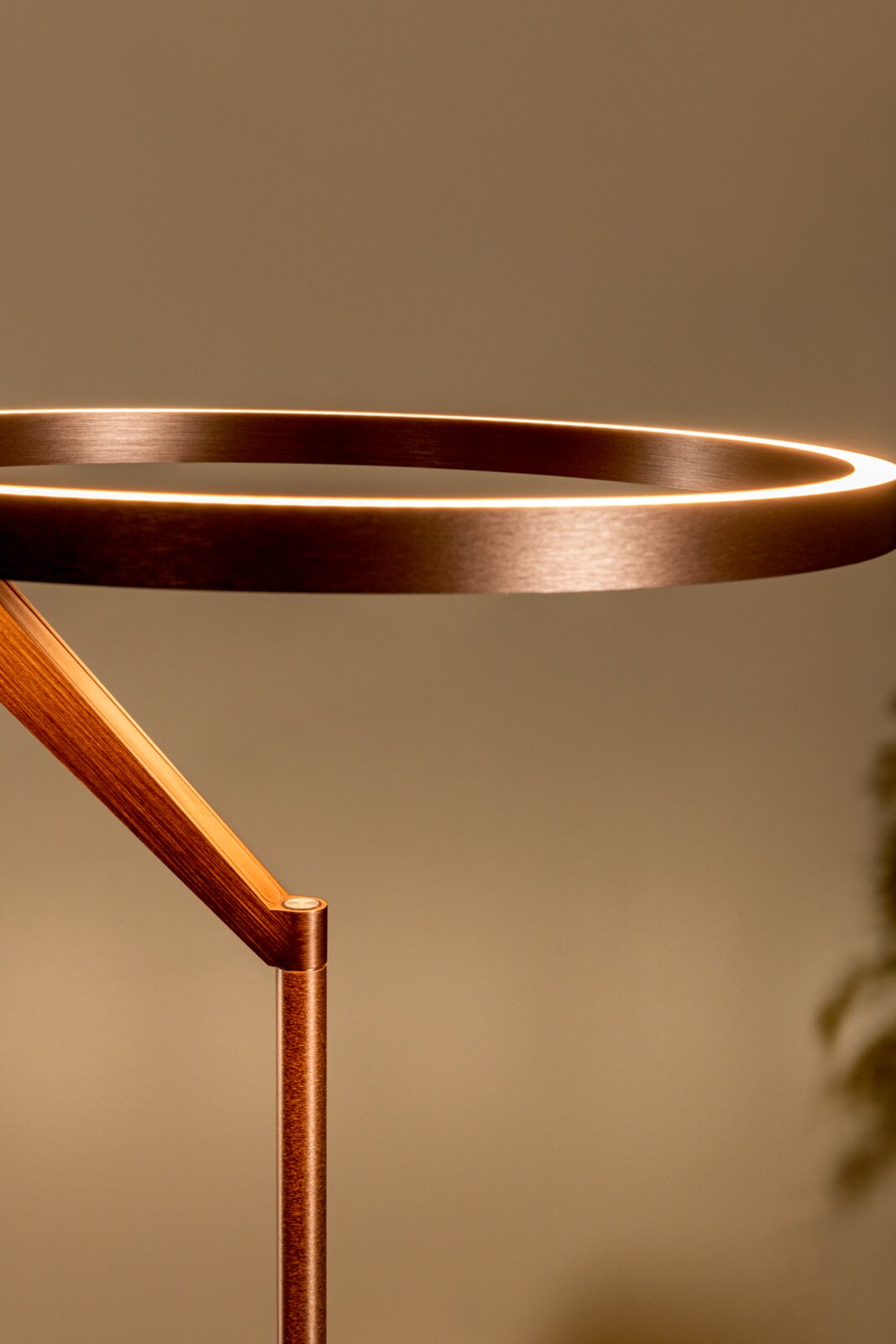 Moderne LED-Stehleuchte mit ringförmigem Leuchtkopf in gebürsteter Metall-Optik, warmweiß leuchtend, Detailansicht aus seitlicher Perspektive vor neutralem Hintergrund