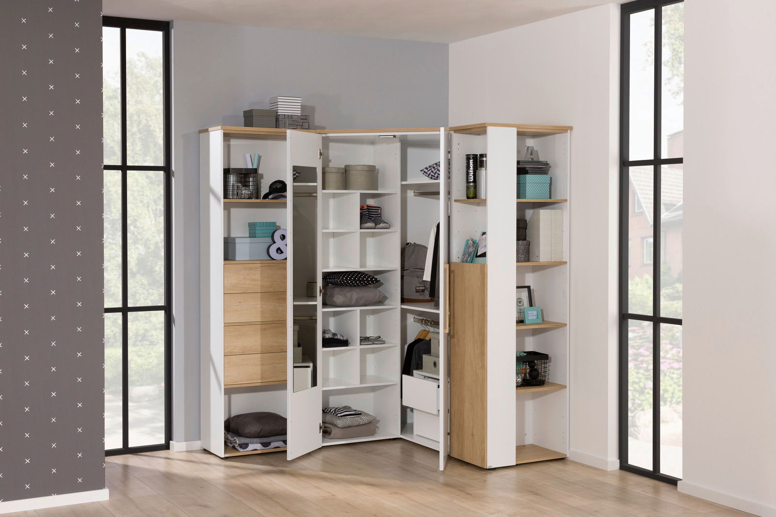 Eck-Kleiderschrank in heller Holzoptik mit offenen und geschlossenen Fächern, gefüllt mit verschiedenen Gegenständen, aus einer frontalen Perspektive fotografiert.