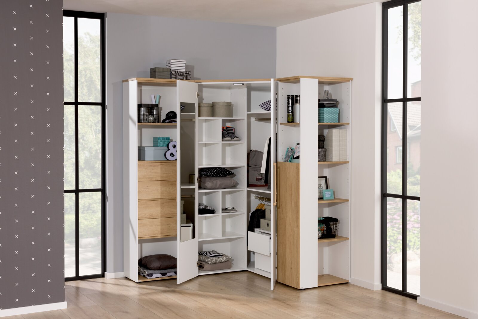 Eck-Kleiderschrank in heller Holzoptik mit offenen und geschlossenen Fächern, gefüllt mit verschiedenen Gegenständen, aus einer frontalen Perspektive fotografiert.