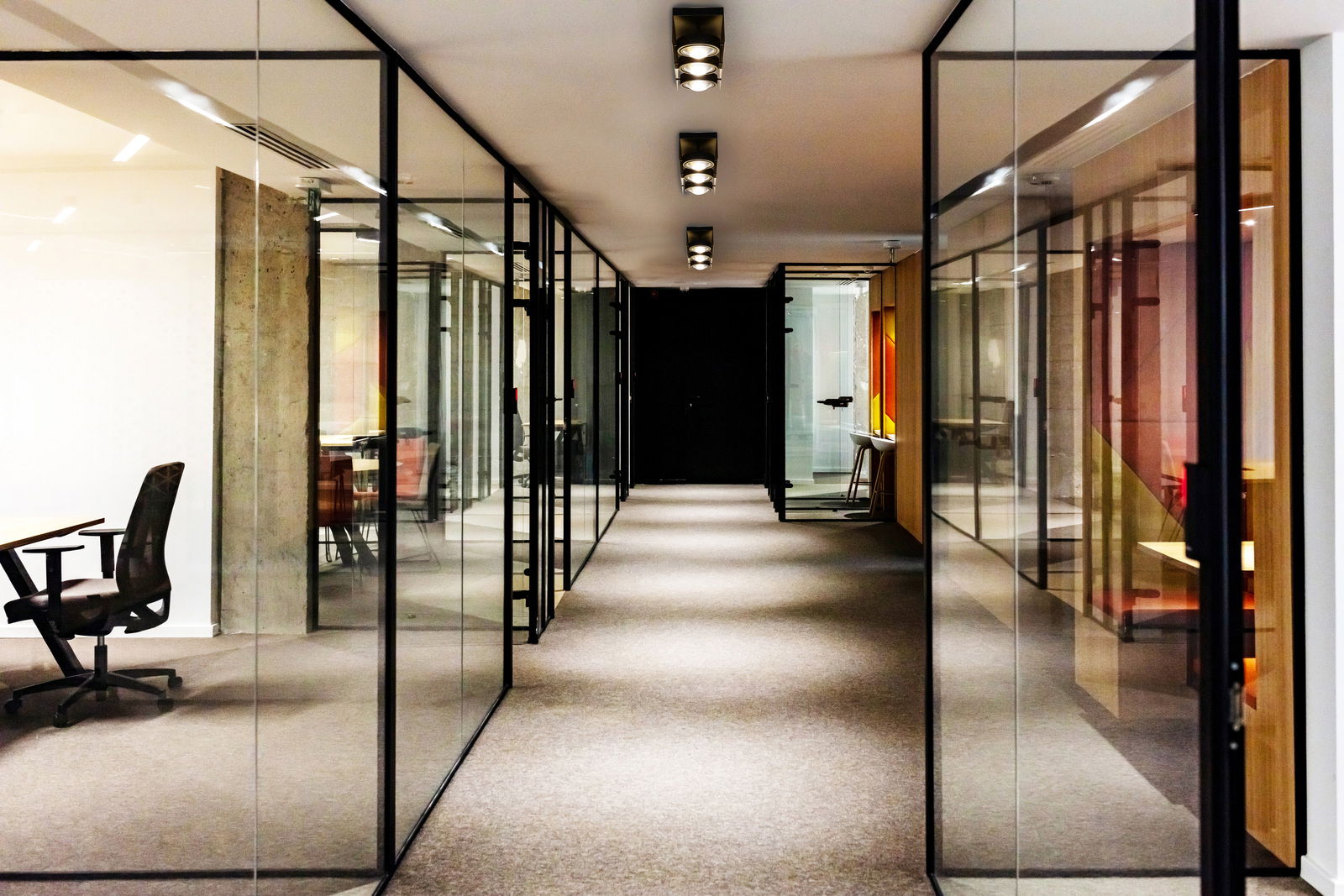 Megatron LED-Deckenleuchte CARDANO Moderne LED-Aufbauleuchten in einem Büroflur mit Glaswänden, aus der Perspektive des Gangs betrachtet.