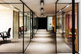 Moderne LED-Aufbauleuchten in einem Büroflur mit Glaswänden, aus der Perspektive des Gangs betrachtet.