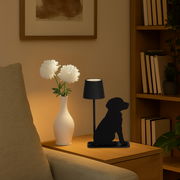 Akku-Tischleuchte in Form eines sitzenden Hundes, seitliche Perspektive, auf einem Tisch neben einer Vase mit weißen Blumen.