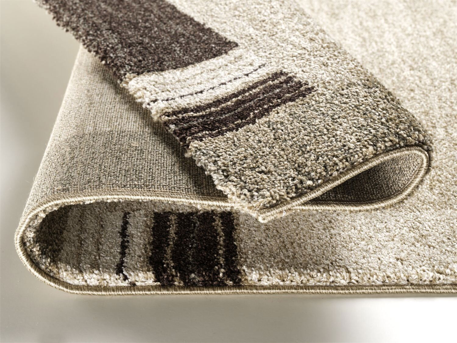 Nahaufnahme eines beigen Teppichs mit braunen Streifen, der an einer Ecke umgeschlagen ist, um die Textur und Dicke zu zeigen.