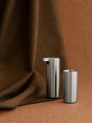 Moderner Seifenspender aus Edelstahl, seitliche Perspektive, vor braunem Stoffhintergrund