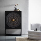 Frontale Ansicht des Highboards SANTA CRUZ mit dekorativem Kreisdesign auf den Türen, daneben ein moderner Sessel.