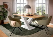 Moderner Esstisch mit Y-förmigem weißen Gestell und Holzplatte, umgeben von grünen Stühlen in einem hellen Esszimmer mit großen Fenstern, aus seitlicher Perspektive.