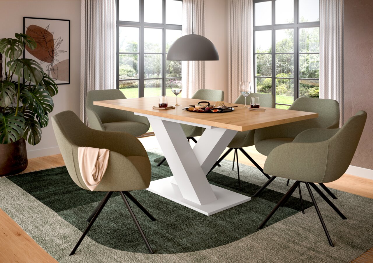 Moderner Esstisch mit Y-förmigem weißen Gestell und Holzplatte, umgeben von grünen Stühlen in einem hellen Esszimmer mit großen Fenstern, aus seitlicher Perspektive.