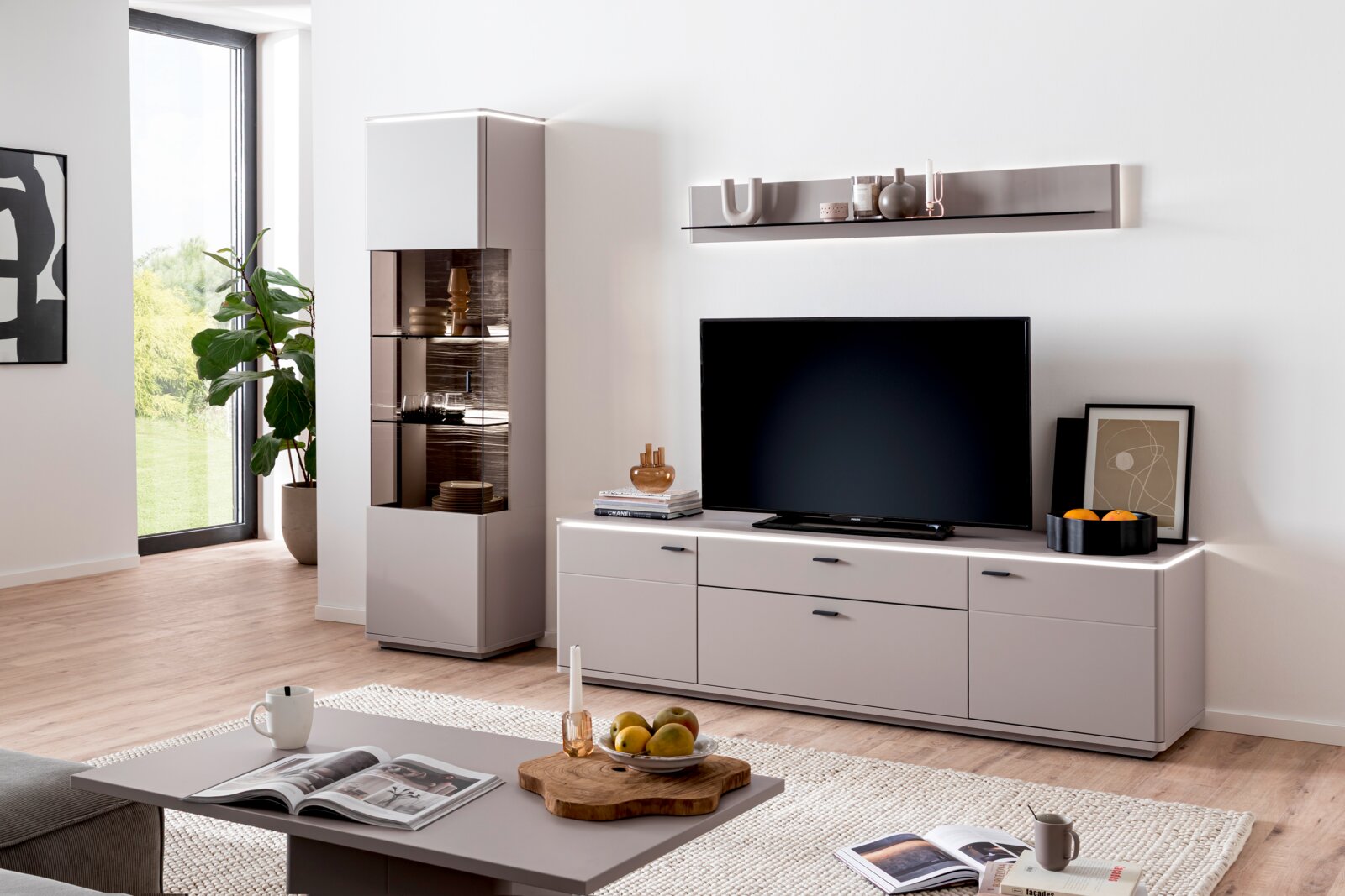 Zurbrüggen Wandkombination TORRENT Modernes Wohnzimmer-Setup mit weißem TV-Lowboard, wandmontiertem Regal und Vitrine mit Glasfront, TV mittig platziert; Perspektive: frontale, leicht seitliche Ansicht auf die Wohnwand.