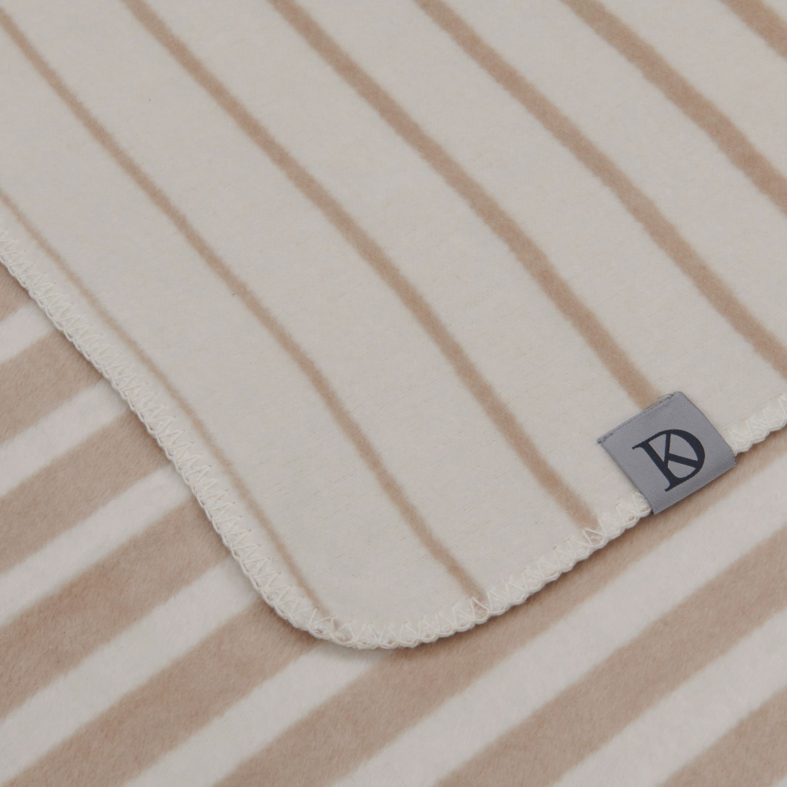 Dieter Knoll Woondeken Nahaufnahme einer gestreiften Wohndecke in Beige- und Weißtönen mit einem Etikett in der Ecke.