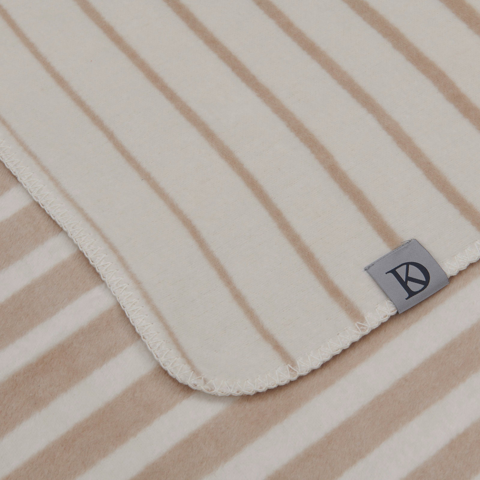 Nahaufnahme einer gestreiften Wohndecke in Beige- und Weißtönen mit einem Etikett in der Ecke.