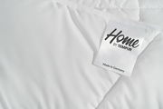 Nahaufnahme einer weißen, gesteppten Decke mit einem Etikett, das 'Home by Tempur' zeigt, perspektivisch von oben.