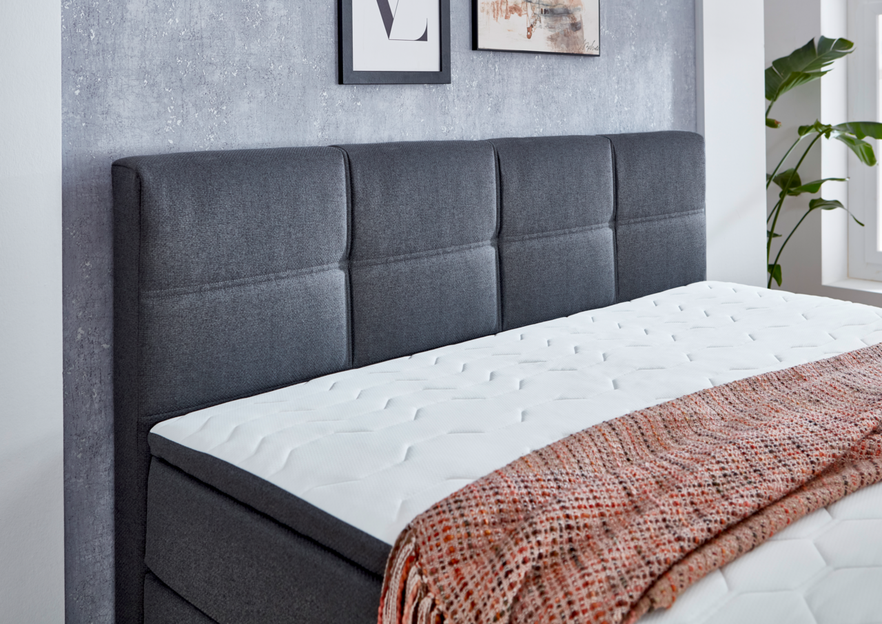 Boxspringbett mit grauem Kopfteil und weißer Matratze, seitliche Perspektive