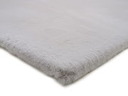 Nahaufnahme eines weichen, hellgrauen Fellteppichs aus der Seitenperspektive.