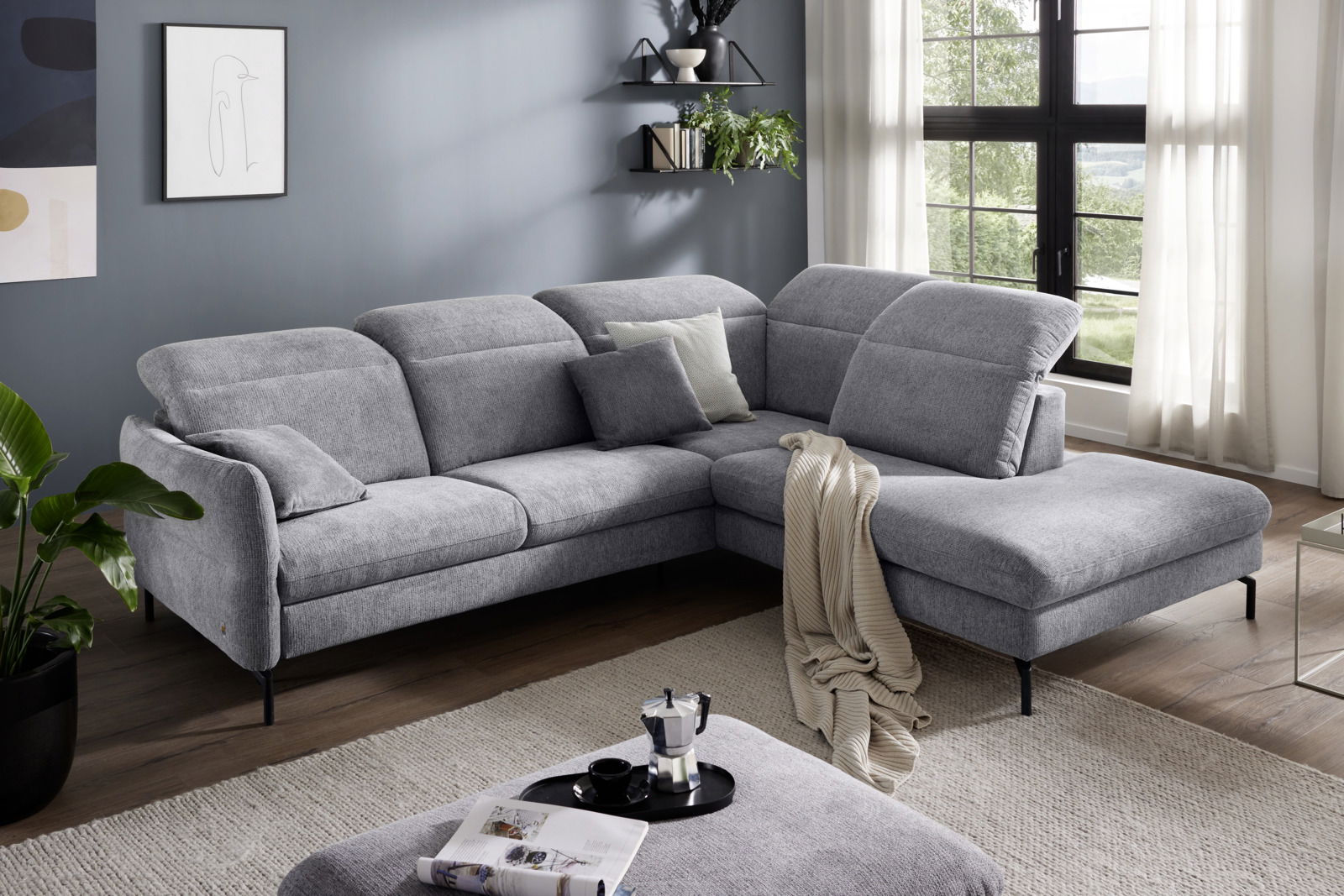 Graue Polsterrundecke in modernem Wohnzimmer, seitliche Perspektive mit großen Fenstern im Hintergrund.