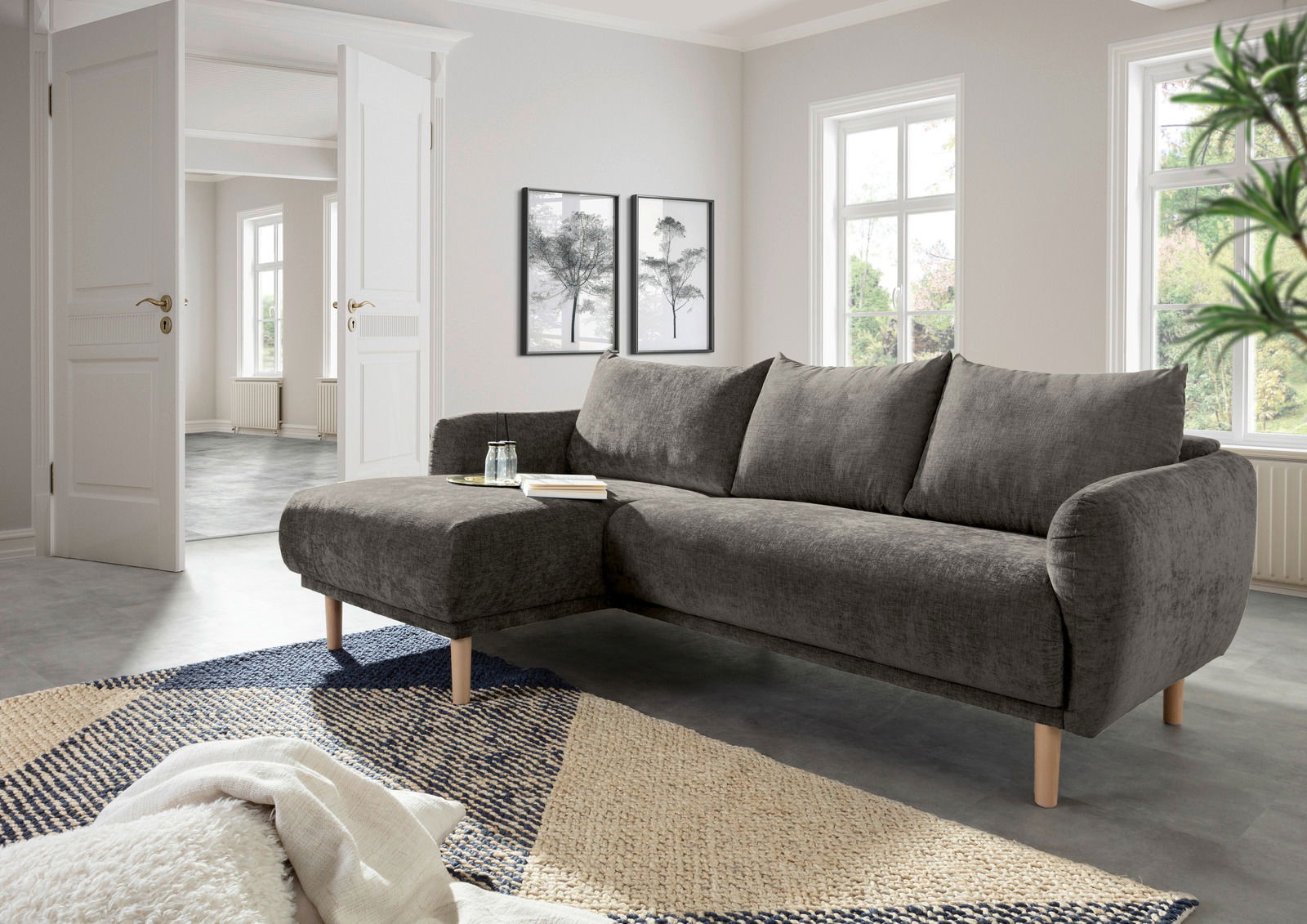 Graues Ecksofa mit Holzfüßen in einem modernen Wohnzimmer, Perspektive von vorne links.