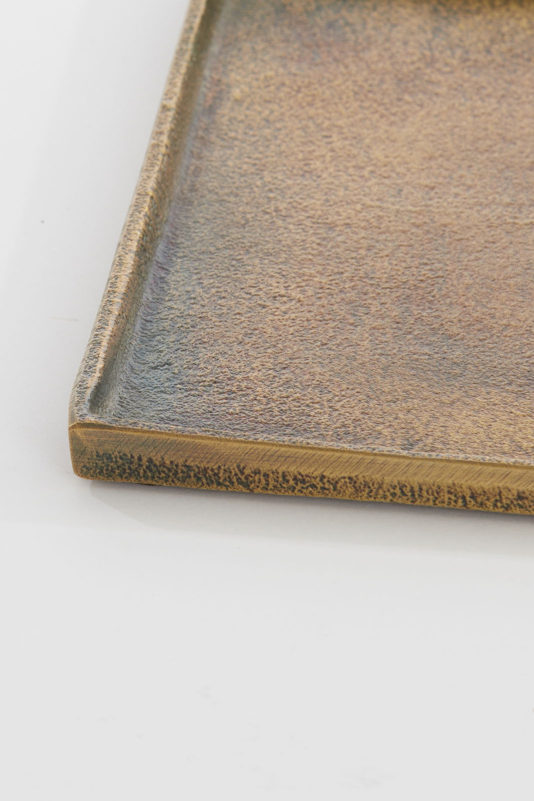 Nahaufnahme einer rechteckigen, flachen Schale mit strukturierter, bronzefarbener Oberfläche, aus der Seitenperspektive fotografiert.