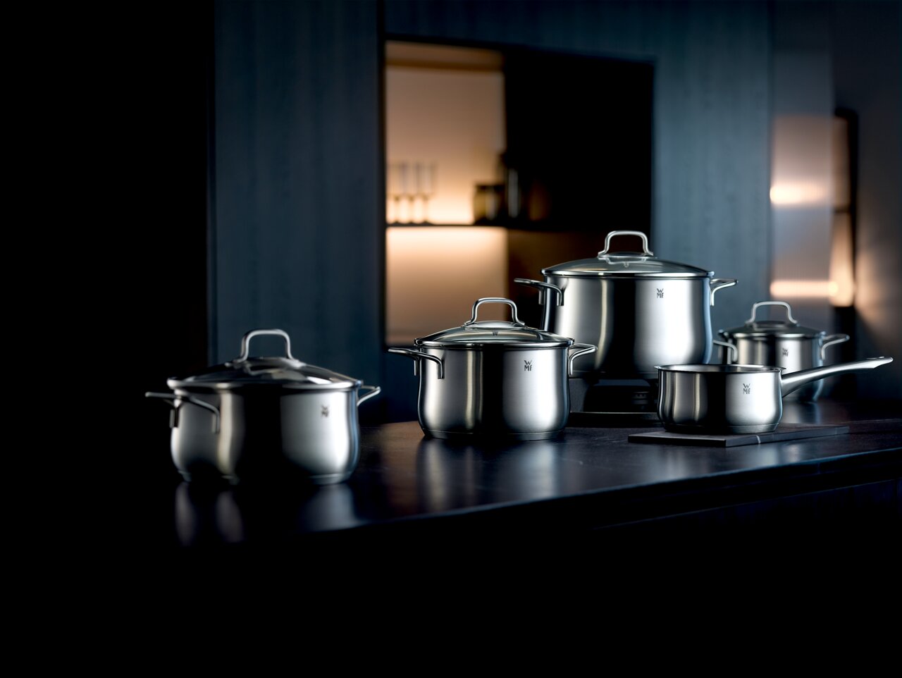 WMF Topfset 4-tlg. BRILLANT Topfset Brillant 4-tlg. aus Edelstahl, bestehend aus drei Töpfen und einer Stielkasserolle, auf einer dunklen Küchenarbeitsplatte in moderner Umgebung, seitliche Perspektive.
