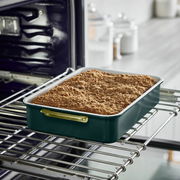 Rechteckige Backform mit goldenen Griffen, gefüllt mit einem gebackenen Kuchen, in einem geöffneten Ofen aus seitlicher Perspektive.