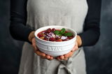 Person hält eine elfenbeinfarbene Schüssel mit frischen Beeren und Minzblättern, Vorderansicht