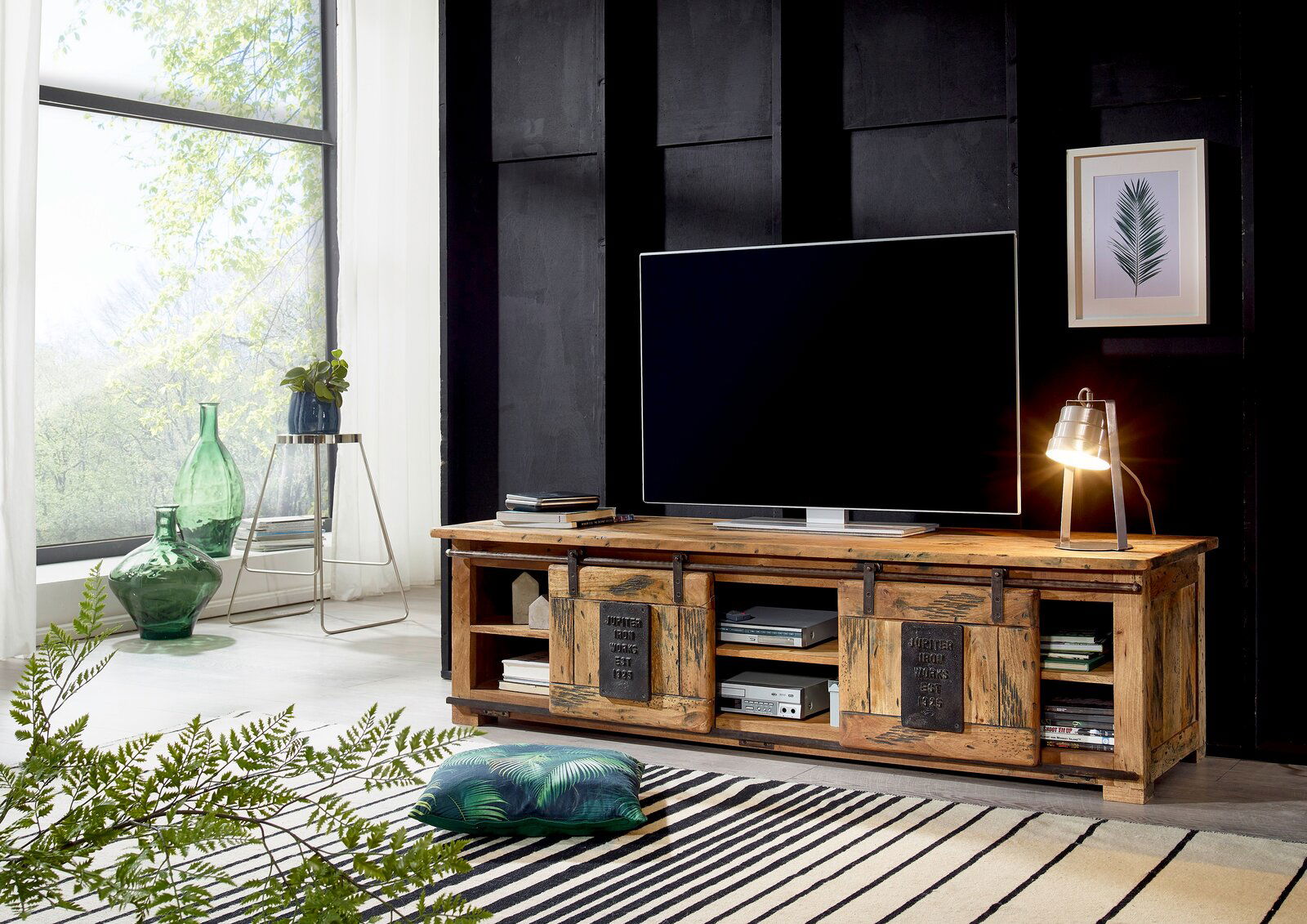 Rustikales TV-Lowboard aus Holz mit Schiebetüren, dekoriert mit einer Tischlampe und einem großen Fernseher, seitliche Perspektive.