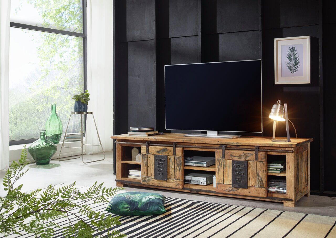 Rustikales TV-Lowboard aus Holz mit Schiebetüren, dekoriert mit einer Tischlampe und einem großen Fernseher, seitliche Perspektive.