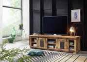 Rustiek houten tv-lowboard met schuifdeuren, versierd met een tafellamp en een grote tv, gezien vanaf de zijkant.
