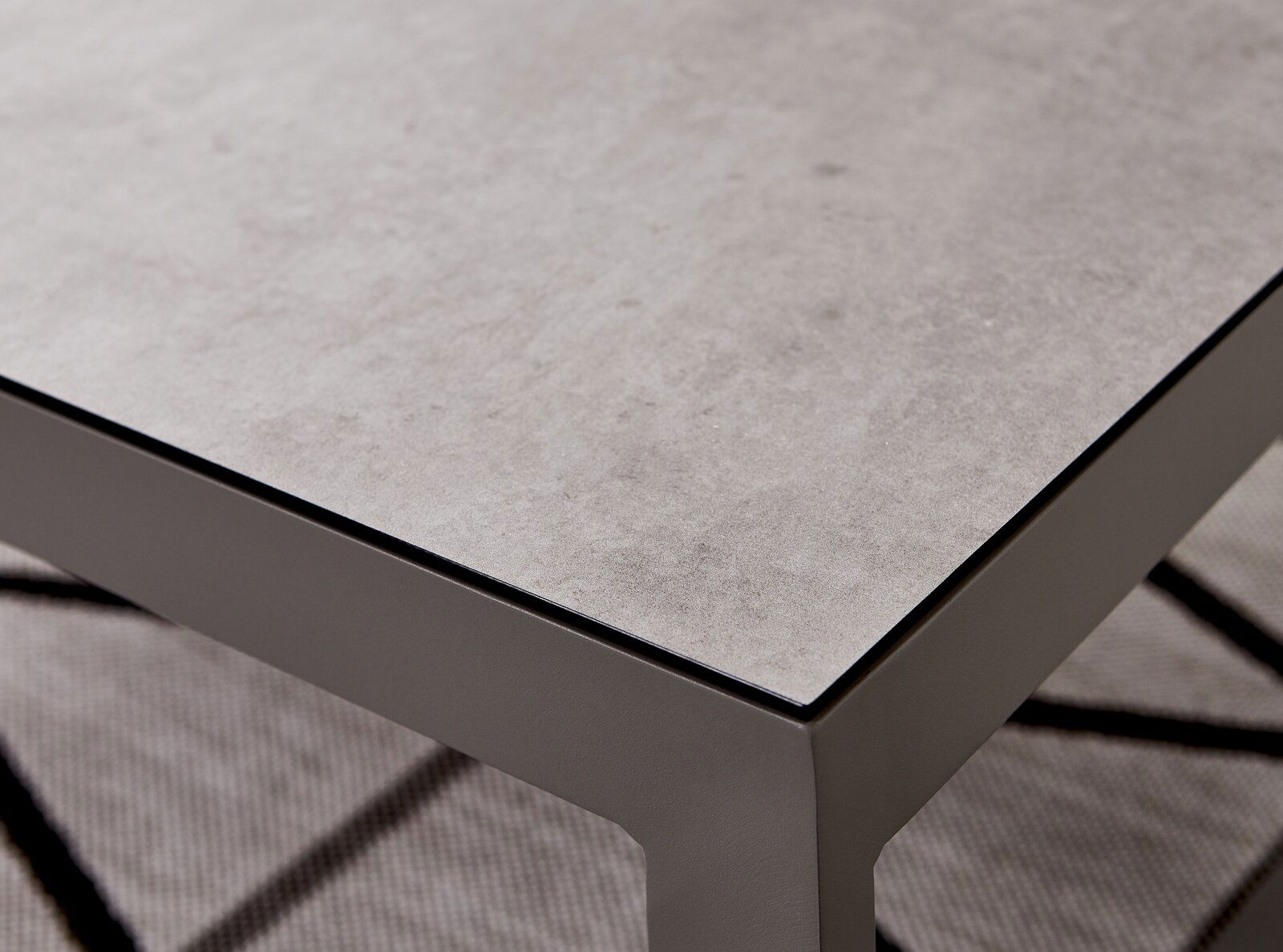 Nahaufnahme eines modernen Lounge-Tisches mit grauer Steinoptik-Oberfläche und stabilen Metallbeinen, perspektivisch von oben rechts fotografiert.