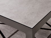Nahaufnahme eines modernen Lounge-Tisches mit grauer Steinoptik-Oberfläche und stabilen Metallbeinen, perspektivisch von oben rechts fotografiert.