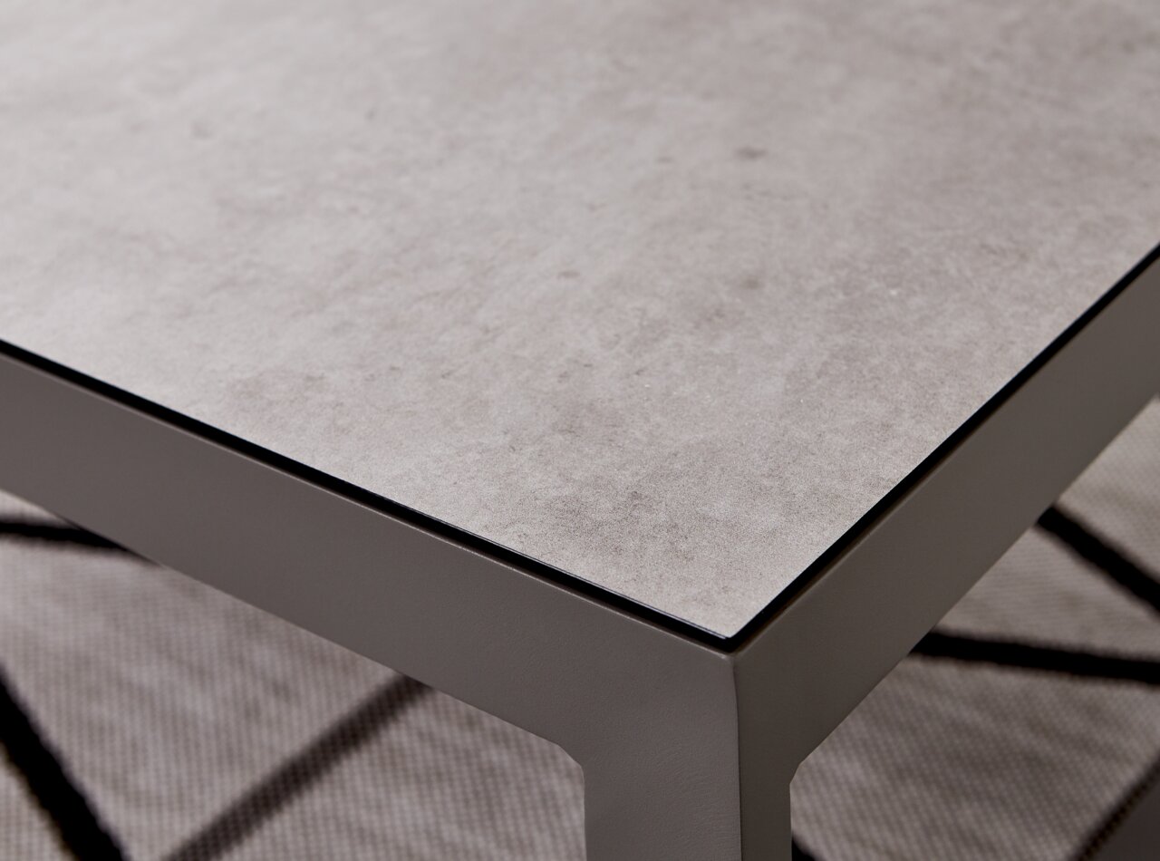 Nahaufnahme eines modernen Lounge-Tisches mit grauer Steinoptik-Oberfläche und stabilen Metallbeinen, perspektivisch von oben rechts fotografiert.