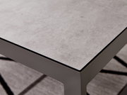 Nahaufnahme eines modernen Lounge-Tisches mit grauer Steinoptik-Oberfläche und stabilen Metallbeinen, perspektivisch von oben rechts fotografiert.