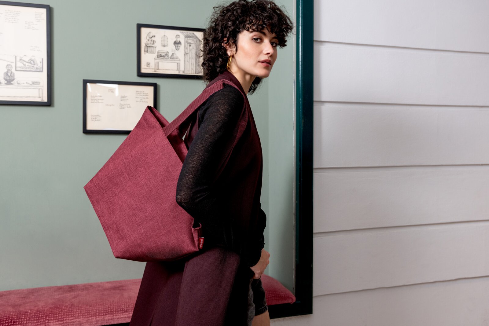 Vrouw met een wijnrode shopper over haar schouder, zijaanzicht