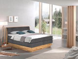 Modernes Boxspringbett in einem hellen Schlafzimmer mit großen Fenstern und Blick auf die Natur, seitliche Perspektive.