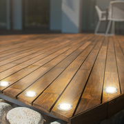 Perspektive von schräg oben auf eine Holzterrasse mit eingebauten Edelstahl-LED-Leuchten, die warmes Licht abstrahlen.