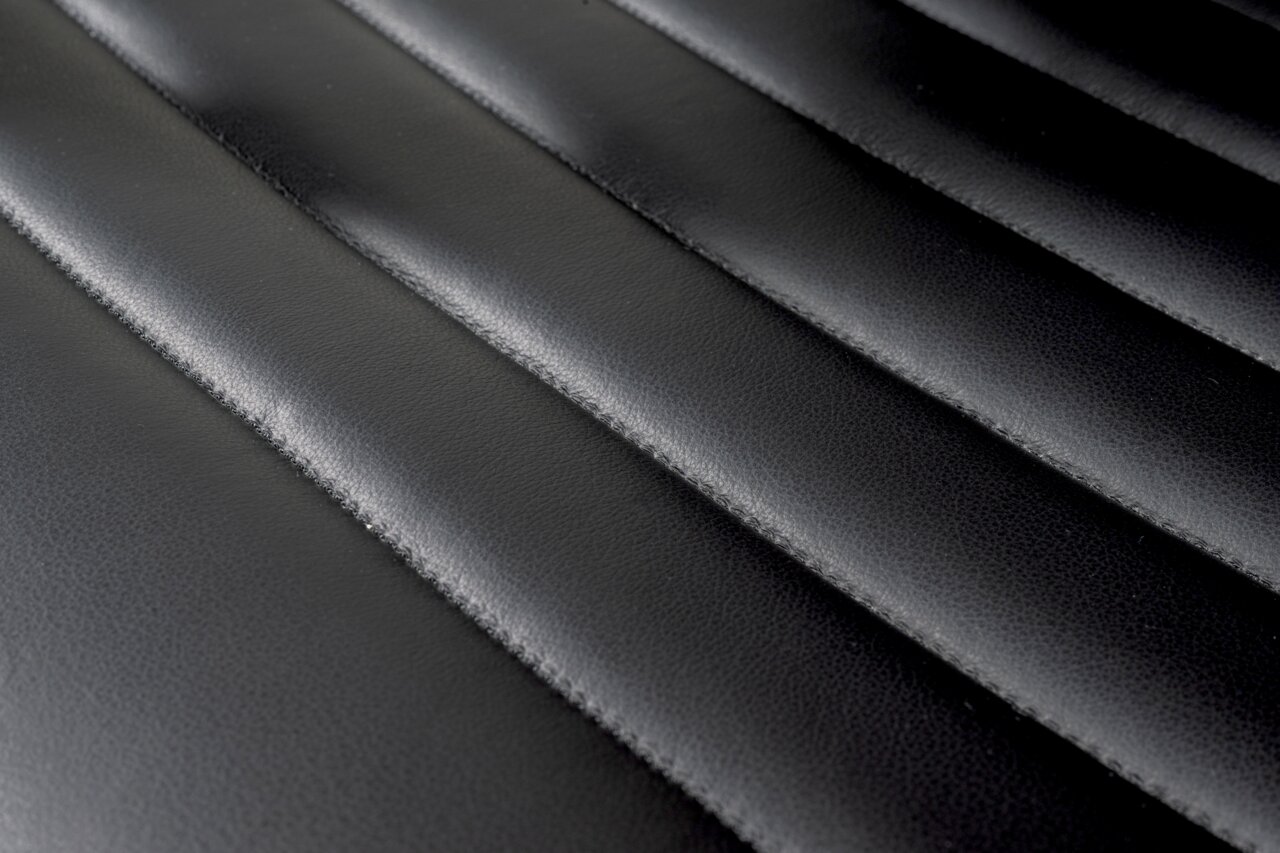 Nahaufnahme der schwarzen, gesteppten Lederoberfläche eines Schwingstuhls, von oben betrachtet.