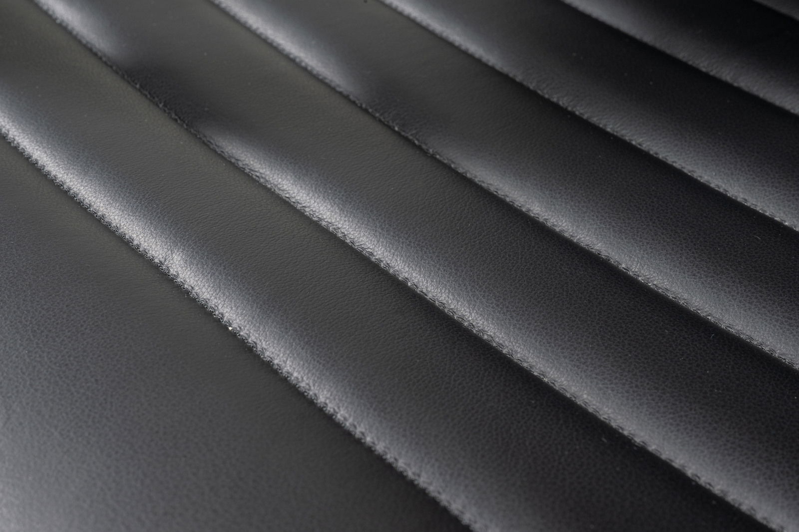 Nahaufnahme der schwarzen, gesteppten Lederoberfläche eines Schwingstuhls, von oben betrachtet.