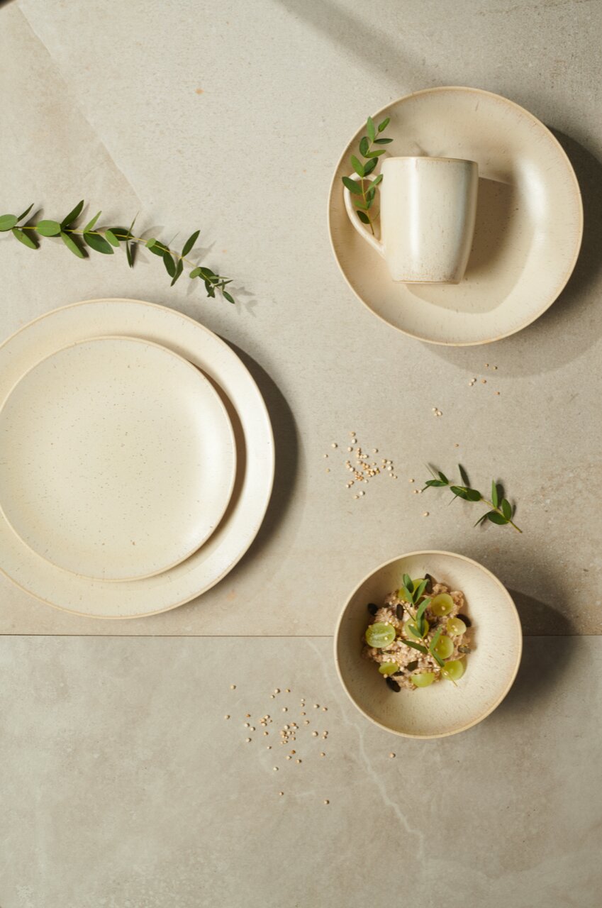 Vogelperspektive auf ein 20-teiliges Kombiservice-Set 'Cafe del' in neutralen Tönen mit Teller, Tasse und Schale, dekoriert mit grünen Blättern.