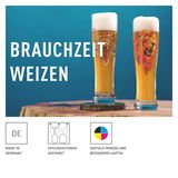 Zwei Weizenbiergläser mit Löwenmotiv, gefüllt mit Bier und Schaumkrone, auf einem Holztisch vor blauem Hintergrund, seitliche Perspektive.