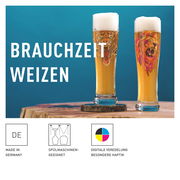 Zwei Weizenbiergläser mit Löwenmotiv, gefüllt mit Bier und Schaumkrone, auf einem Holztisch vor blauem Hintergrund, seitliche Perspektive.