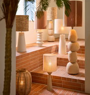 Eine Sammlung von dekorativen Lampen auf einer Treppe mit Terrakottafliesen, darunter ein Lampenfuß mit natürlicher Holzoptik. Die Perspektive zeigt die Lampen von der Seite.