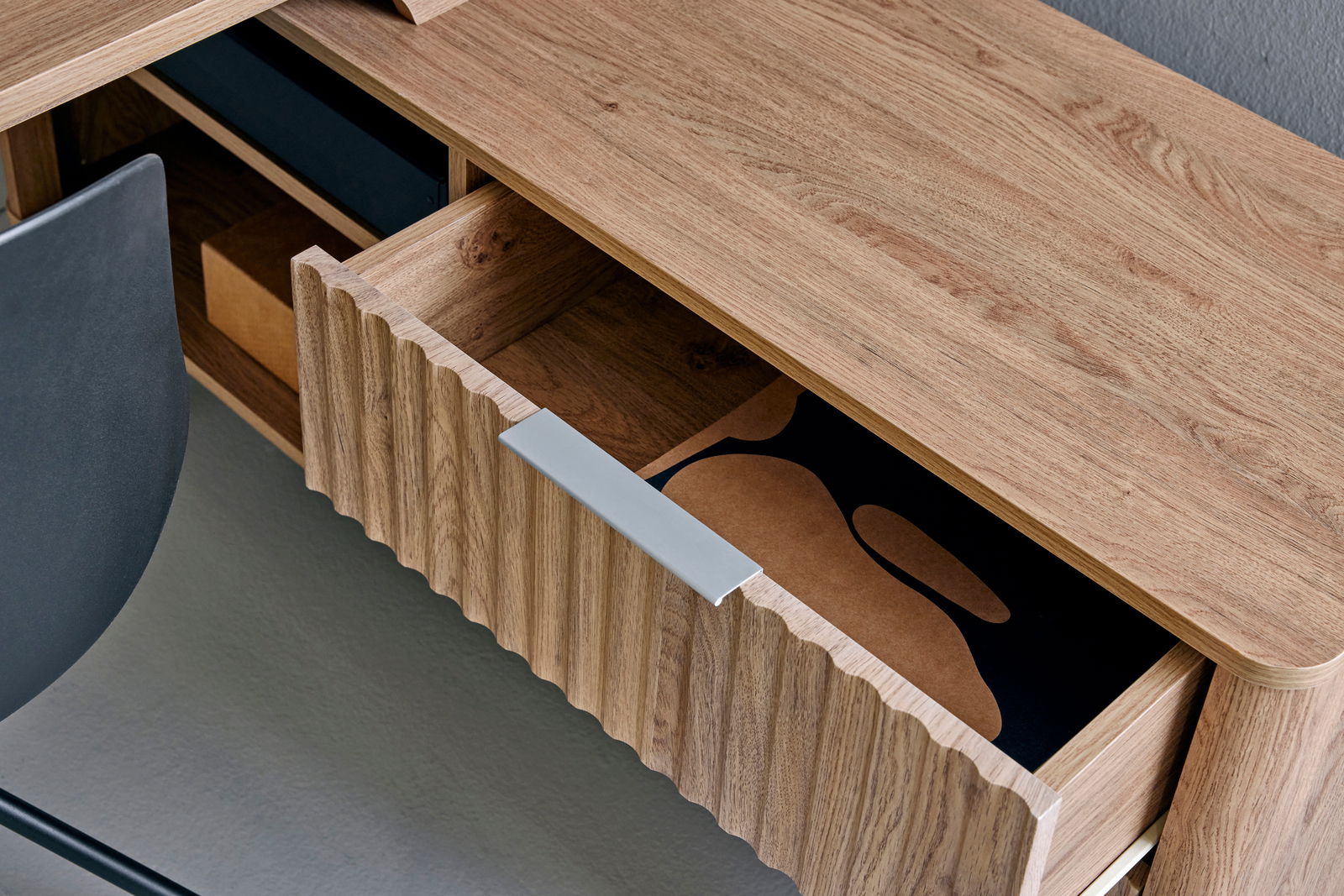 Nahaufnahme eines Eck-Schreibtisches aus Holz mit geöffneter Schublade, von oben fotografiert.