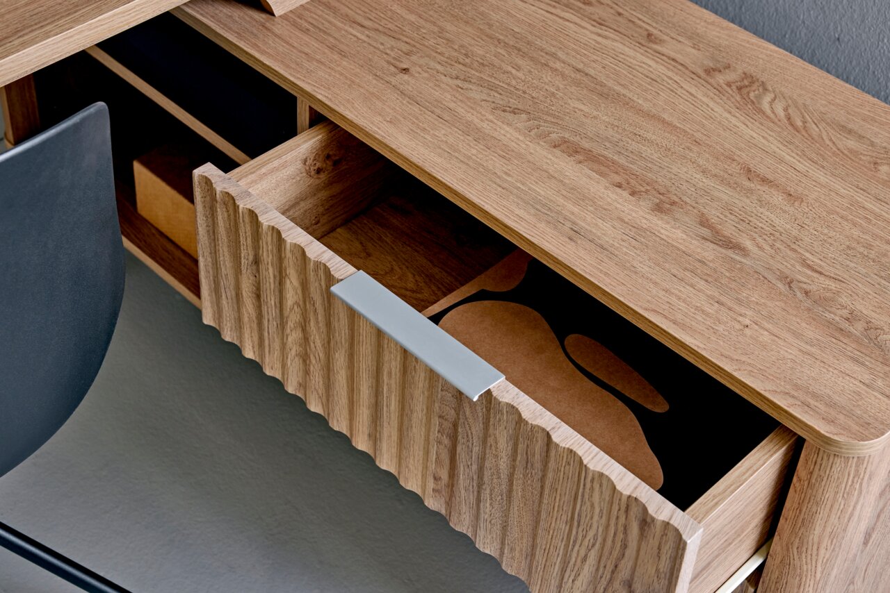 Nahaufnahme eines Eck-Schreibtisches aus Holz mit geöffneter Schublade, von oben fotografiert.
