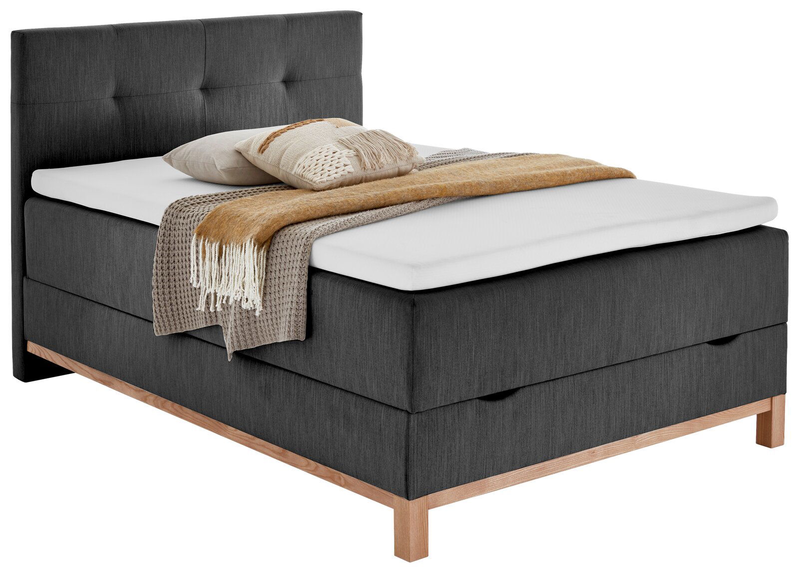 Graues Boxspringbett mit Holzfüßen, dekoriert mit Kissen und Decken, seitliche Perspektive