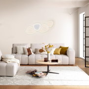 Modernes Wohnzimmer mit beigem Sofa und Couchtisch; an der Wand leuchtet eine abstrakte, mehrteilige LED-Wandleuchte in warmweiß, frontal aus leicht erhöhter Perspektive fotografiert.