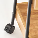 Nahaufnahme eines schwarzen Rollwagens mit Holzablage, Fokus auf das Rad und die Struktur.