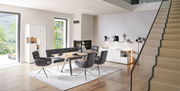 Modernes Esszimmer mit Esstisch, grauen Stühlen und Sideboard in heller, offener Raumgestaltung, seitliche Perspektive.