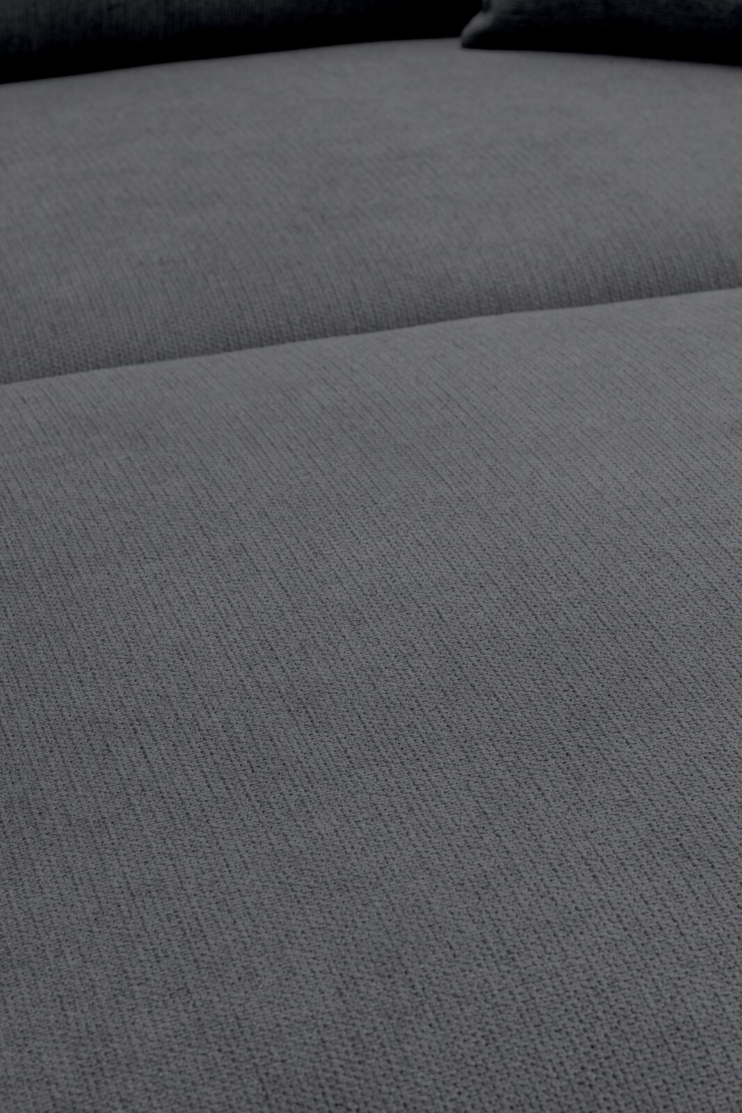 Nahaufnahme der grauen, strukturierten Polsteroberfläche eines Sofas, aufgenommen aus schräger Draufsicht.