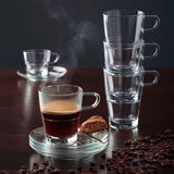 Espressotasse Senso 70ml mit dampfendem Espresso, von vorne fotografiert, auf einem Tisch mit Kaffeebohnen und einem Keks auf der Untertasse.