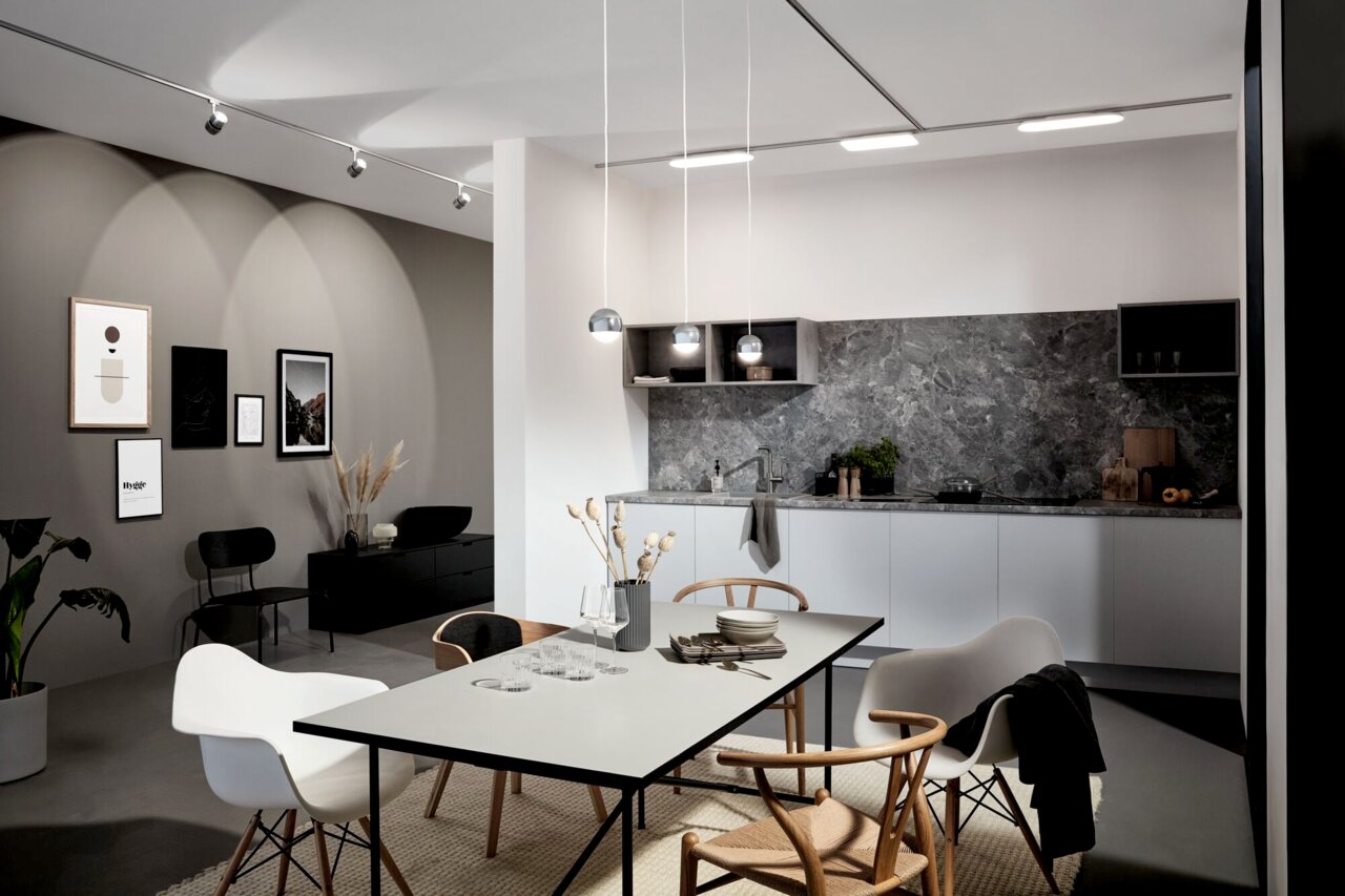 Moderne Küche mit grauem Marmor-Backsplash und drei hängenden Schienenpendelleuchten in Kugelform, Perspektive von der Seite.