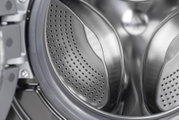 Nahaufnahme der Edelstahltrommel einer Waschmaschine mit gelochten Mitnehmern, Ansicht schräg von vorn in den Innenraum