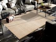 Beige Wollteppich in einem modernen Wohnzimmer, umgeben von einem grauen Sofa, einem Couchtisch und einer Ledertasche auf einem schwarz-weißen Marmorboden. Perspektive von oben.